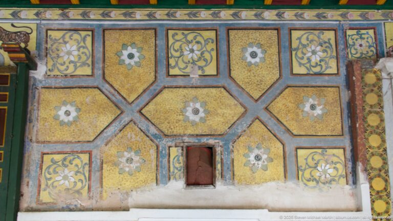 Decorated palace wall with ochre geometric panels, floral medallions, scrolling motifs, and a small recessed opening near the base.