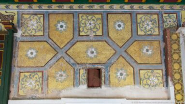 Decorated palace wall with ochre geometric panels, floral medallions, scrolling motifs, and a small recessed opening near the base.