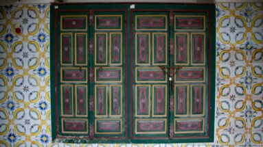 Green double doors with red floral panels set within white tiles decorated with looping yellow and green motifs.
