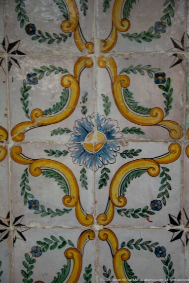 Four-tile floral composition with central blue rosette, curling yellow scrolls, green leaves, and small colored blossoms.