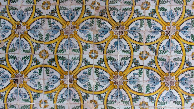 Wall of glazed tiles with interlocking yellow ovals, blue-gray leaves, green stems, and small floral motifs.