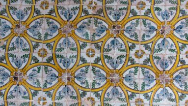 Wall of glazed tiles with interlocking yellow ovals, blue-gray leaves, green stems, and small floral motifs.