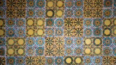 Close wall detail combining yellow circular medallions, blue-brown rosettes, and star-like floral patterns in ceramic tiles.
