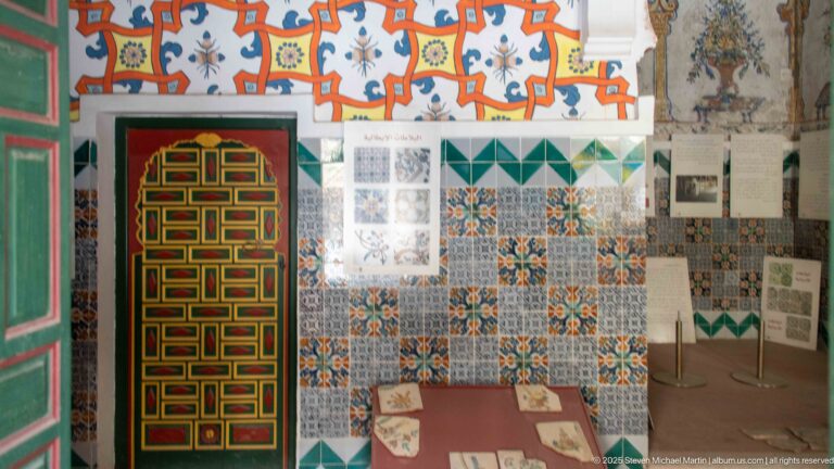 Museum display with explanatory panels, tile patterns, a glass-topped case, and a brightly painted geometric palace door.
