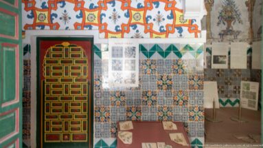 Museum display with explanatory panels, tile patterns, a glass-topped case, and a brightly painted geometric palace door.