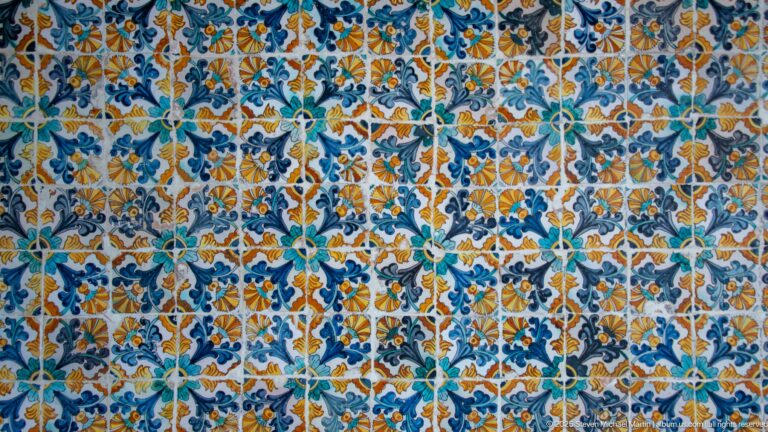 Close view of repeating blue, turquoise, green, ochre, and white floral-patterned ceramic tiles.