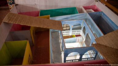 Overhead view of a colorful cutaway architectural model with rooms, galleries, roof sections, and a central courtyard.