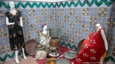 Female mannequins in traditional garments displayed with large trays, pots, bowls, and household vessels against patterned tiles.