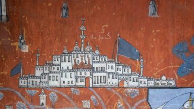 Red-ground mural of a domed architectural complex with towers, flags, surrounding buildings, and Arabic writing above.