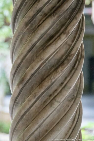 Close-up of a pale stone column shaft carved with deep continuous spiral fluting.