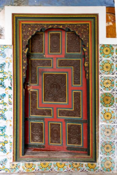 Small multicolored geometric paneled door surrounded by patterned ceramic tiles at Ahmed Bey Palace.