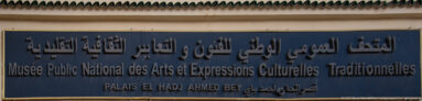 Blue exterior museum sign with Arabic and French lettering naming the National Public Museum and Palais El Hadj Ahmed Bey.