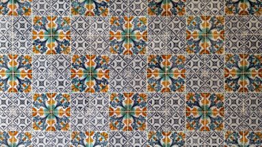Tile wall with repeating blue, green, and orange floral medallions alternating across a fine black-and-white geometric pattern.
