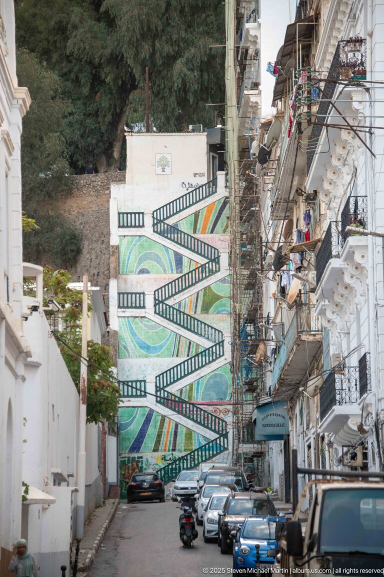 Steep Algiers street ending at a large colorful stair mural with filmstrip-like geometric borders.