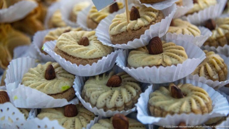 Small pale pastries in paper cups, each molded with ridges and topped with a whole almond.