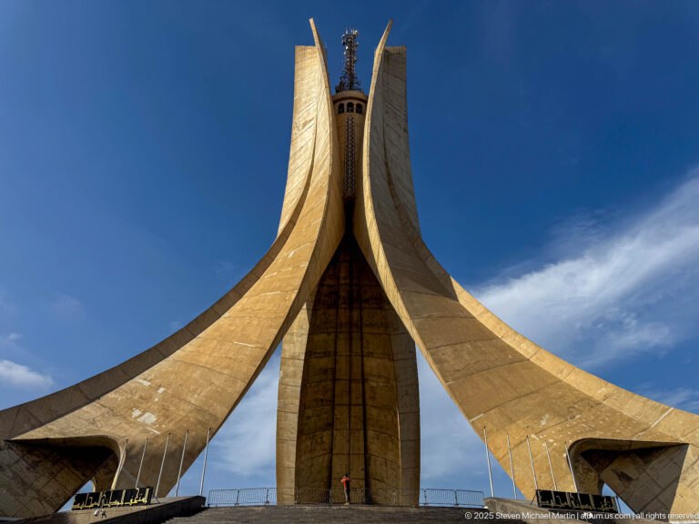 Symmetrical full-height view of the Martyrs’ Memorial rising above broad steps under blue sky.