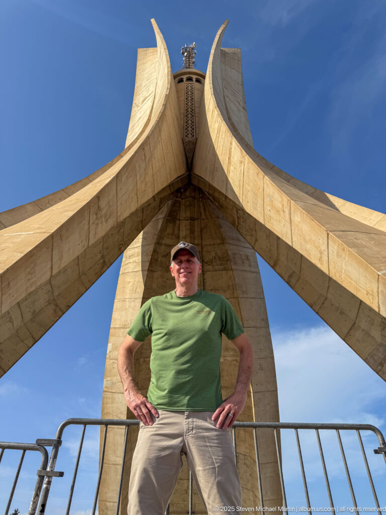 Man standing beneath the curving concrete fins of the Martyrs’ Memorial in Algiers.