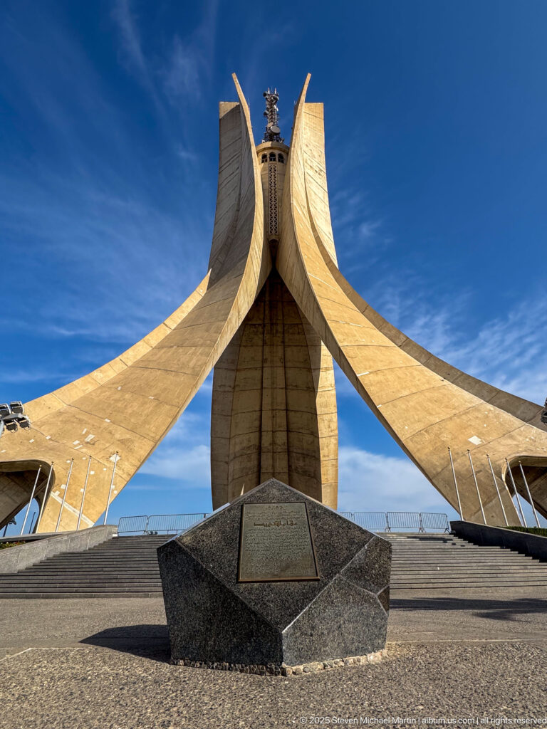 Low-angle view beneath the three curving concrete fins of the Martyrs’ Memorial against blue sky.