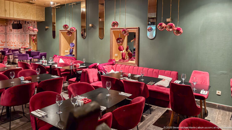 Wide restaurant interior with red seating, dark tables, mirrors, and hanging spherical glass decorations.