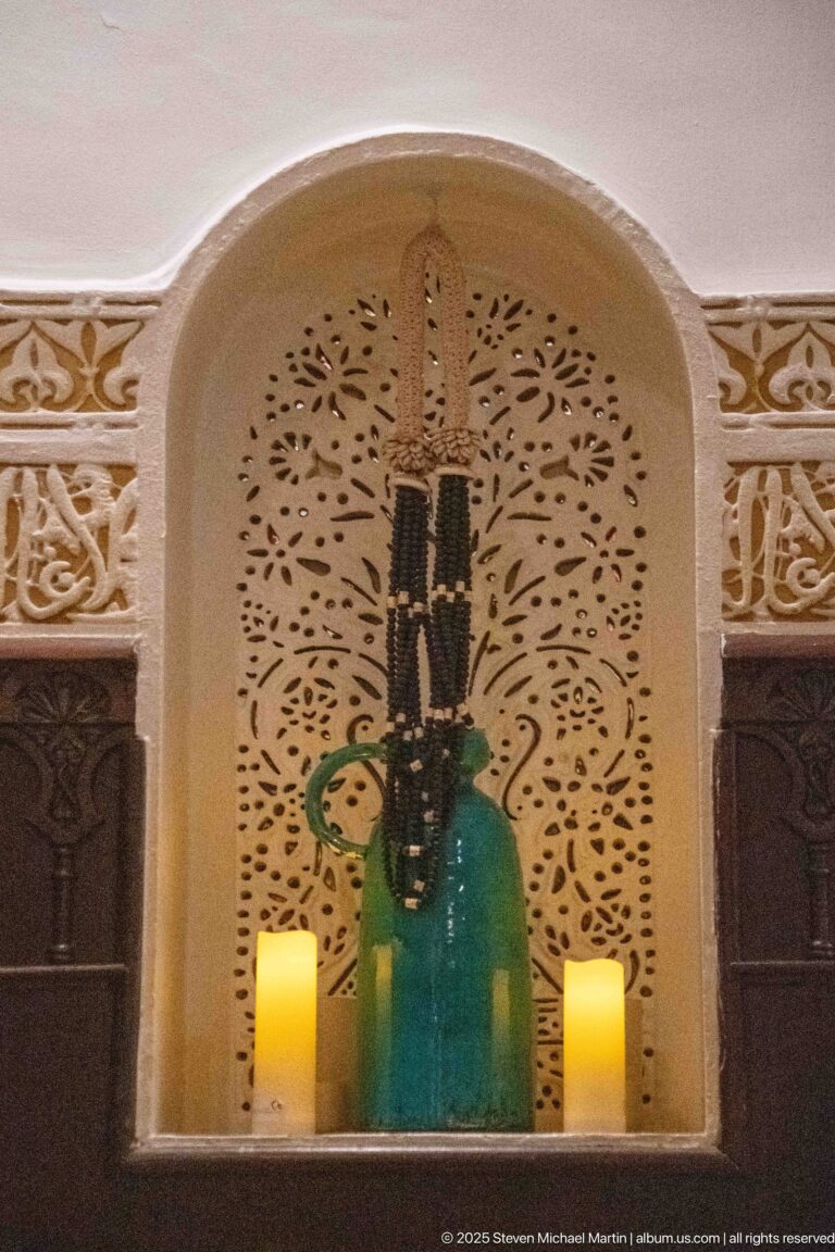 Decorative wall niche with pierced pale plasterwork, a large green glass vessel, and two small glowing candles.