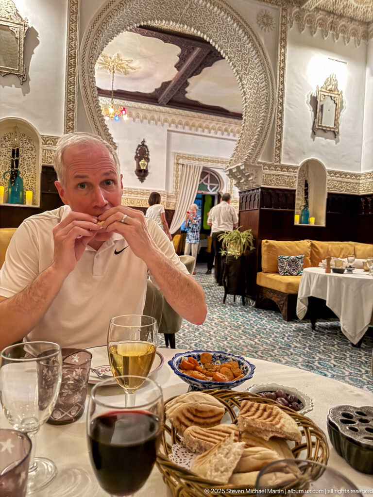 Man eating flatbread at a restaurant table with glasses and small dishes beneath an ornate horseshoe arch.