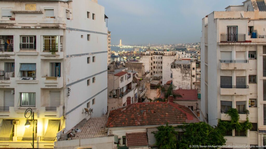 White apartment buildings and tiled rooftops overlooking dense Algiers neighborhoods at dusk.