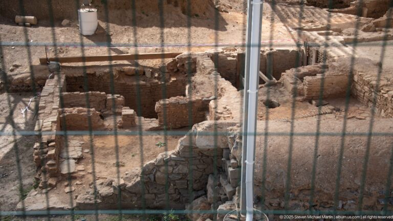 Excavated stone and brick foundations behind a wire fence at an archaeological site in Algiers.