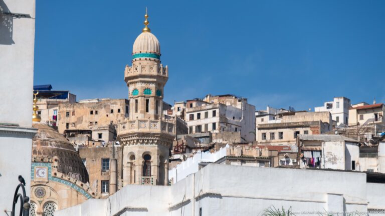 Ornate minaret with turquoise accents and domed crown rising above dense historic buildings in Algiers.