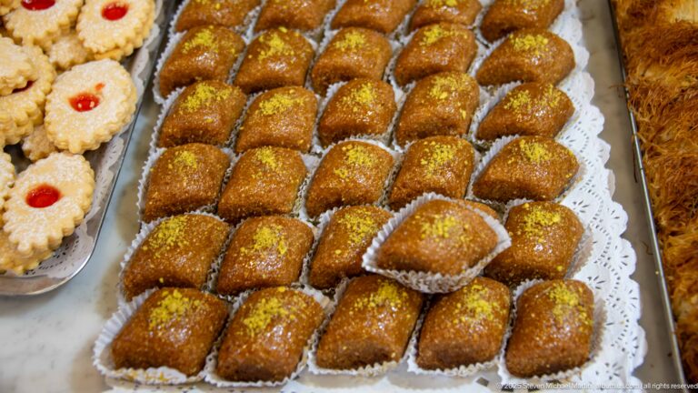 Tray of glossy golden-brown pastries in paper cups, each dusted with green pistachio.