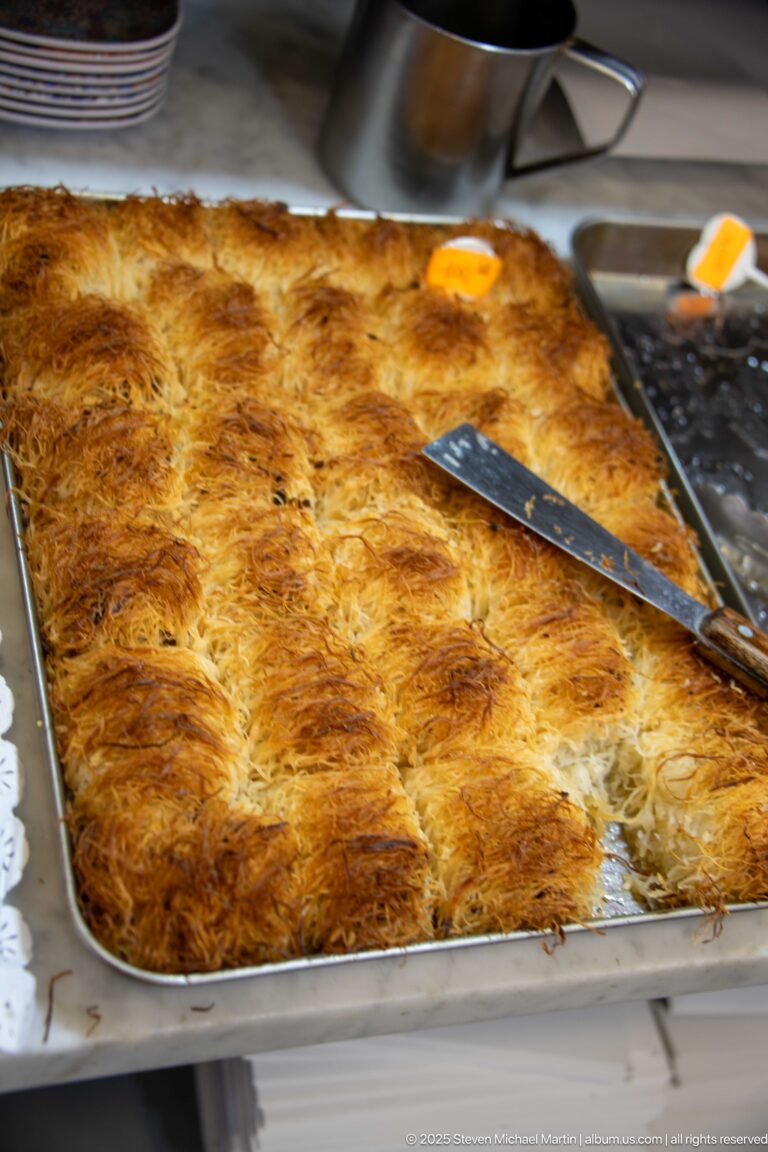 Large rectangular tray of browned shredded pastry cut into portions with a knife resting on top.