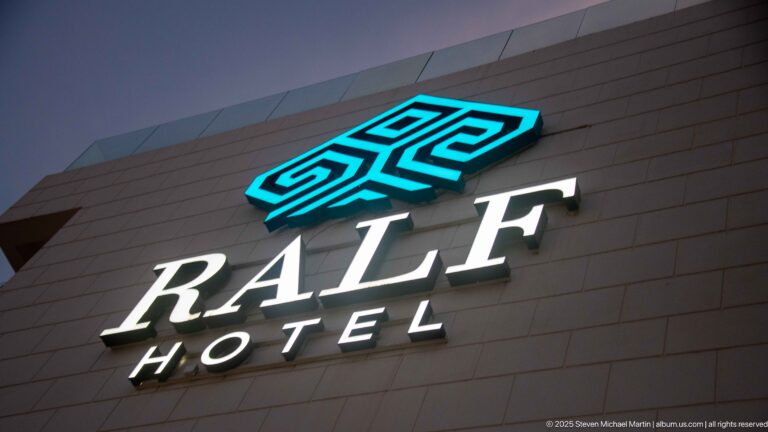 Illuminated RALF HOTEL sign with turquoise logo and white lettering on a dark modern façade at night.