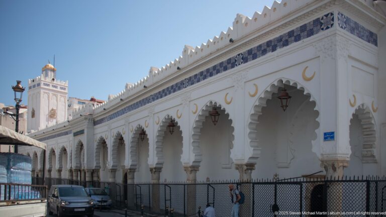 Long white arcaded building with scalloped arches, gold crescent motifs, blue trim, and a square tower.