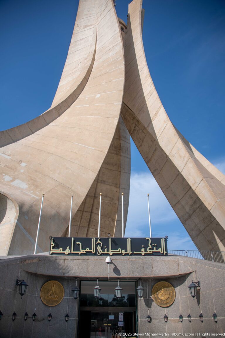 Entrance beneath the concrete fins of the Martyrs’ Memorial with gold Arabic lettering above the doorway.
