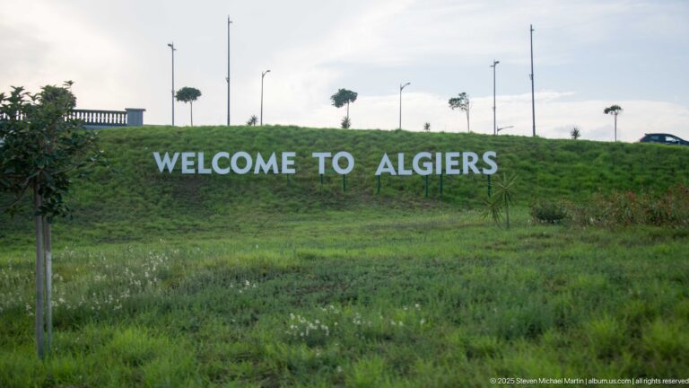 Large white WELCOME TO ALGIERS letters across a grassy roadside embankment.