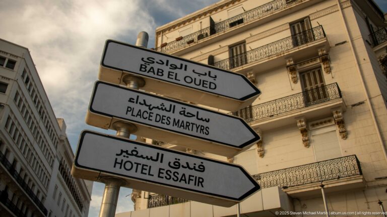 Arabic-and-French directional signs for Bab El Oued, Place des Martyrs, and Hôtel Essafir against historic buildings.