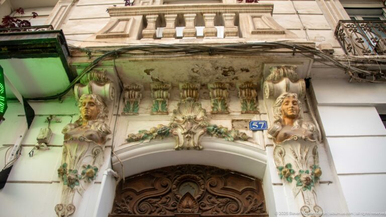 Ornate doorway with sculpted female figures, floral reliefs, carved wooden door, and address number 57.