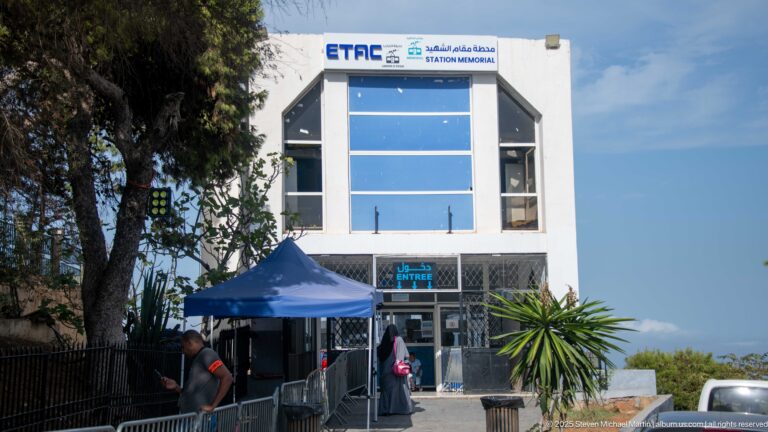 Modern ETAC Station Mémorial building with blue glass façade, entrance sign, railings, and pedestrians.