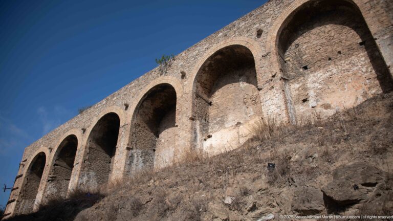 Low-angle view up a weathered masonry structure with a sequence of large rounded arched recesses.