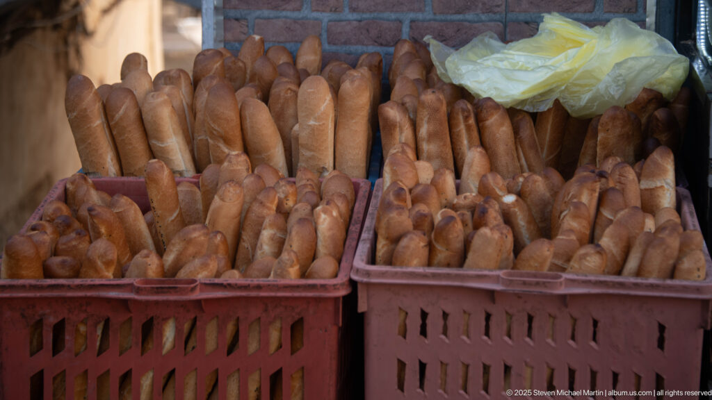 Plastic crates densely filled with long golden-brown bread loaves at a market or bakery.
