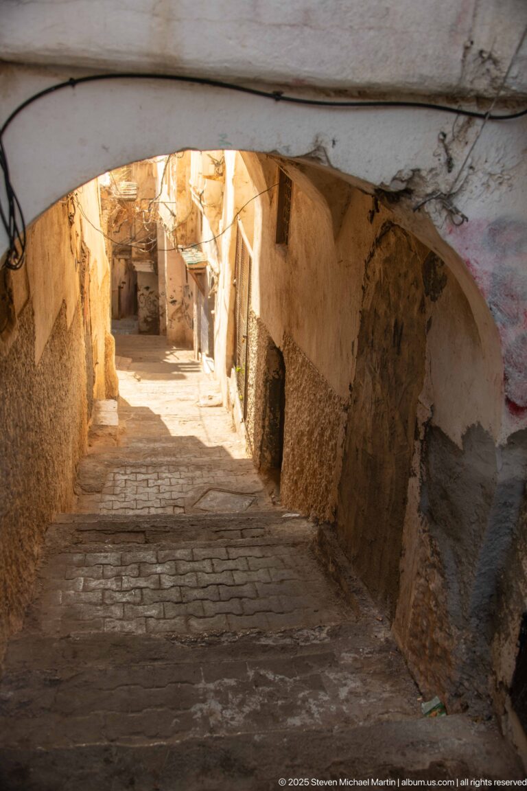 Stone steps descending beneath a low white arch through a narrow, weathered Casbah passage.