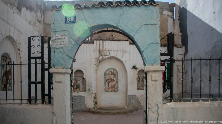 Turquoise and white arched doorway behind black railings, with small decorative panels set into the surrounding wall.