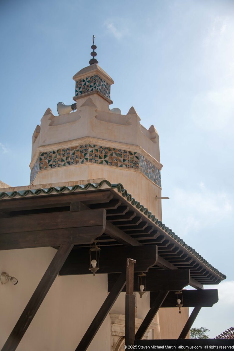 Low-angle view of a pale rooftop structure with blue-green geometric decoration, timber eaves, and a small finial.
