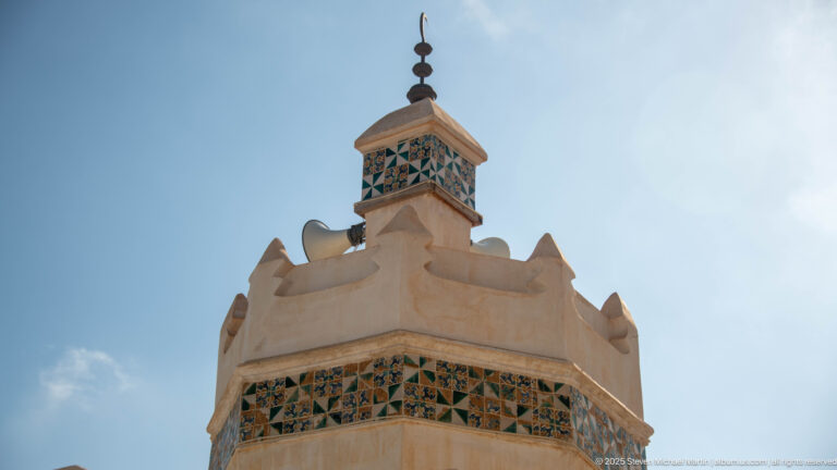 Close low-angle view of a pale rooftop tower with blue-green geometric panels, shaped parapet, and dark finial.