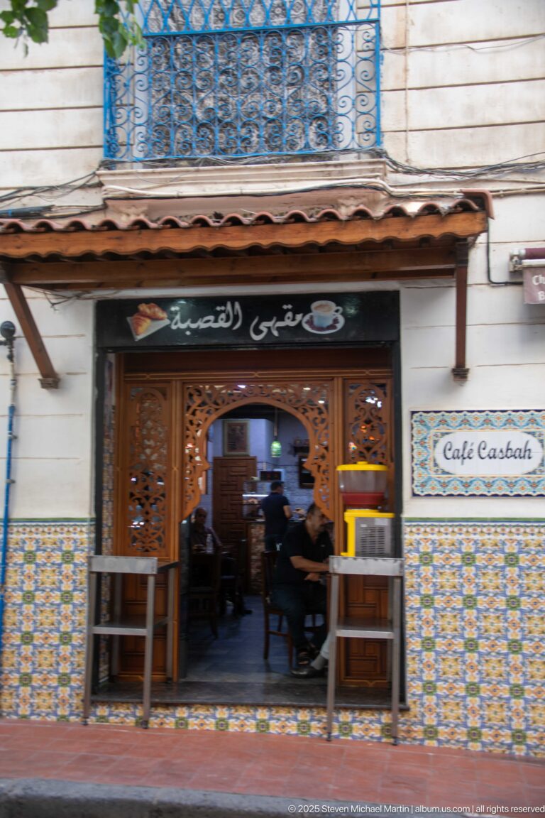 Ornate wooden entrance to Café Casbah framed by patterned tiles, with patrons seated inside.