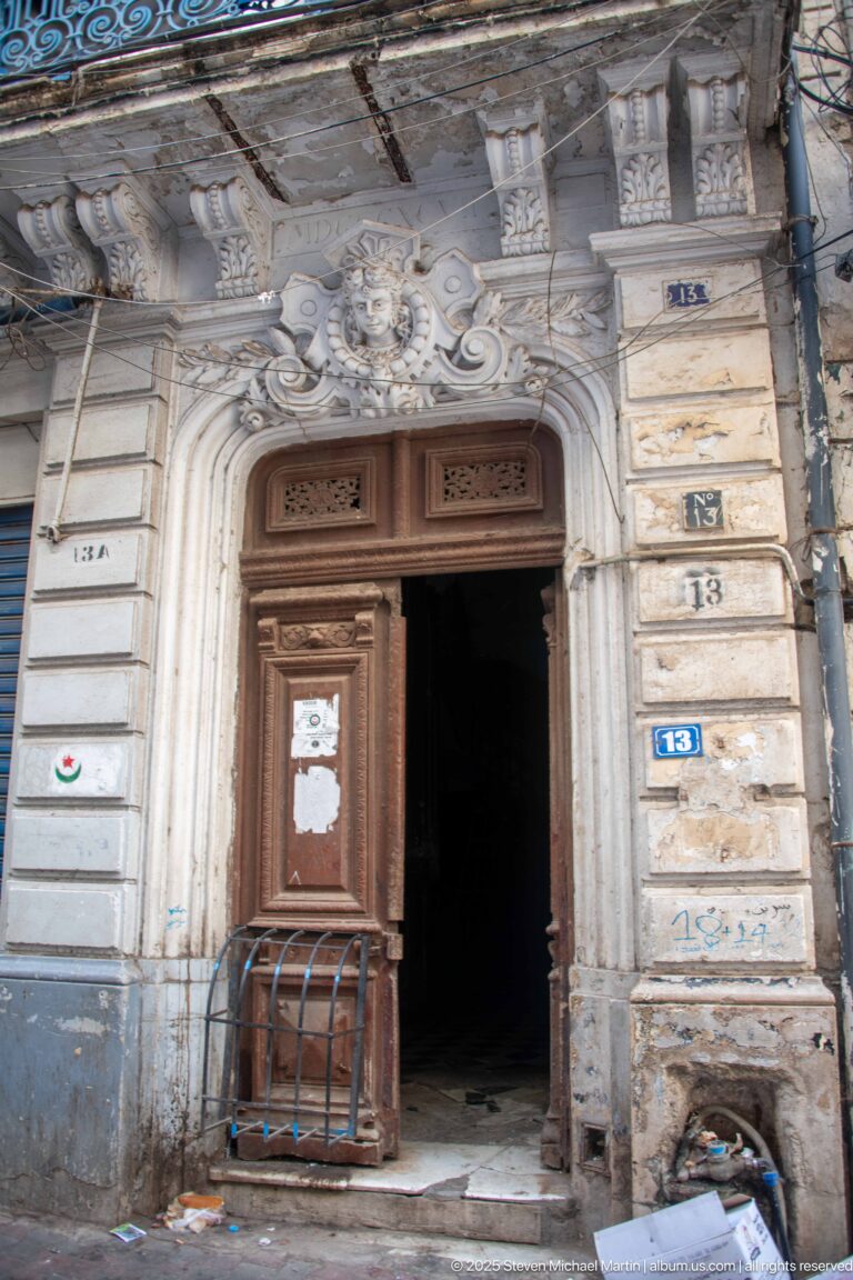 Ornately carved stone doorway with tall brown wooden doors and sculpted floral decoration above the arch.