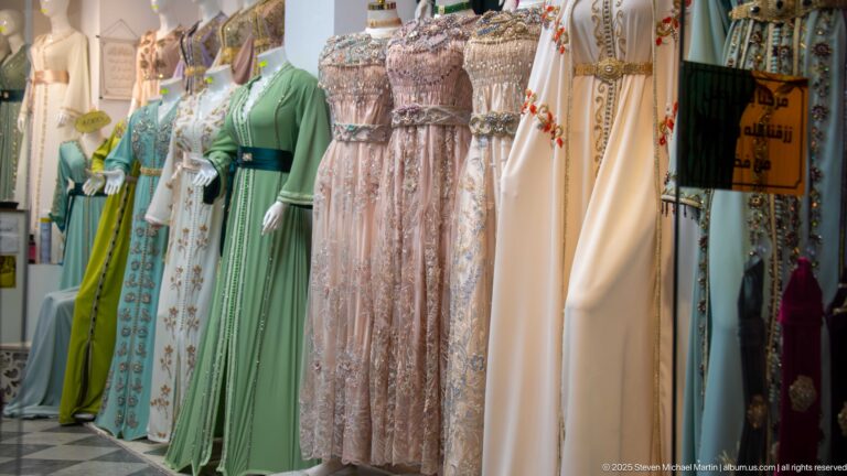 Pastel green, cream, pink, and white embroidered long dresses displayed on mannequins inside a Casbah clothing shop.