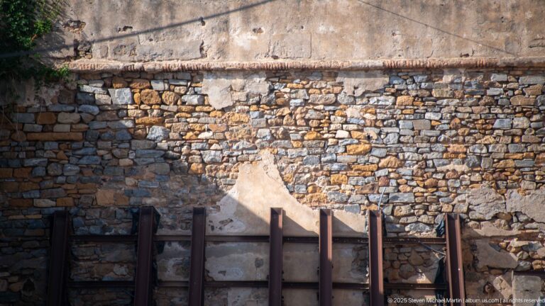 Close view of a weathered Casbah wall built of small stones and plaster, with heavy dark timber supports at its base.