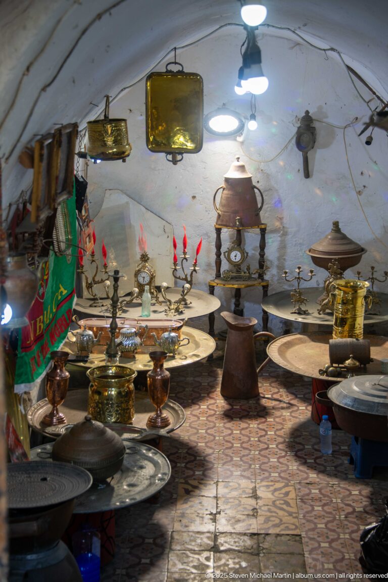 Casbah shop interior filled with brass- and copper-colored trays, tables, candlesticks, lidded vessels, and hanging metalware.
