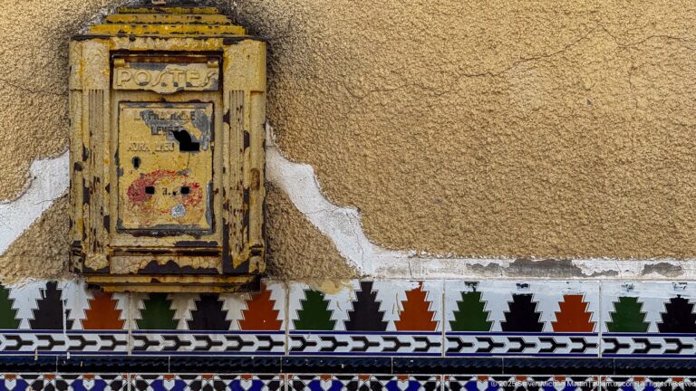 Weathered metal utility box on an ochre wall above green, red, black, white, and blue geometric tile bands.