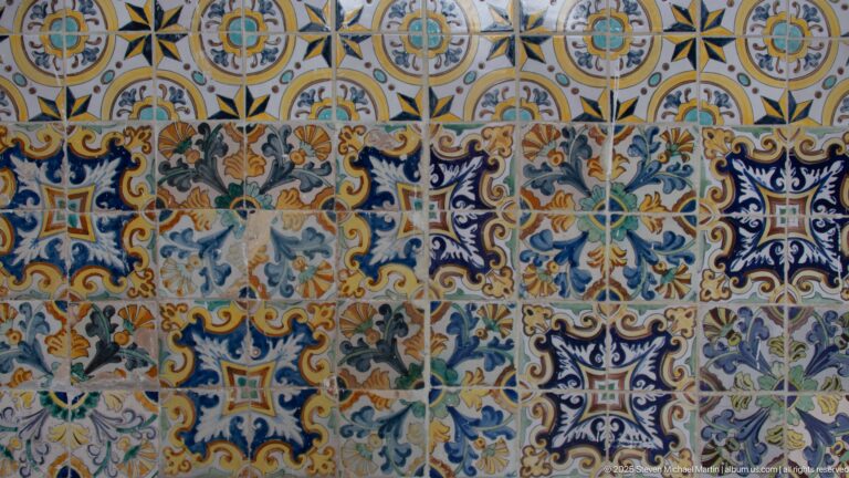 Close view of multicolored ceramic tiles with blue scrolling foliage, geometric compartments, and yellow, green, orange, and white details.